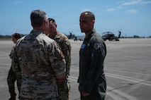 Three service members stand on the flightline talking to each other.