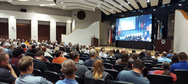 A group of people seated in auditorium watch a screen.