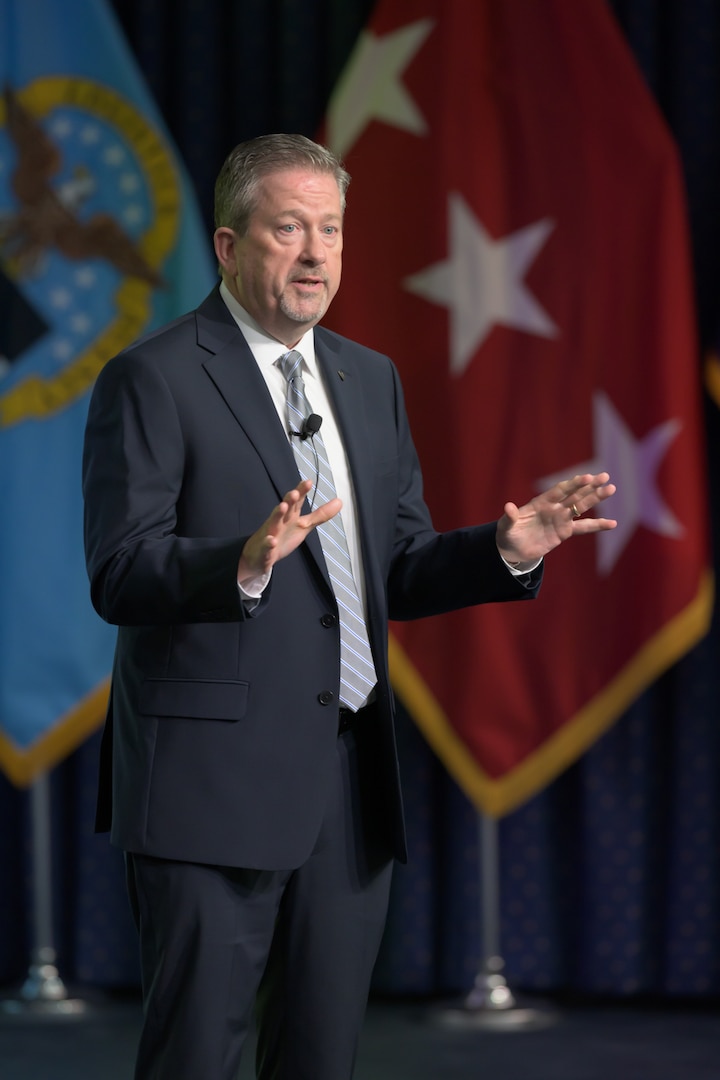 A man wearing a suit speaks on a stage.