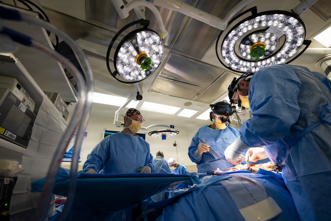 Three medical personnel perform surgery in an operating room under dim spotlights.