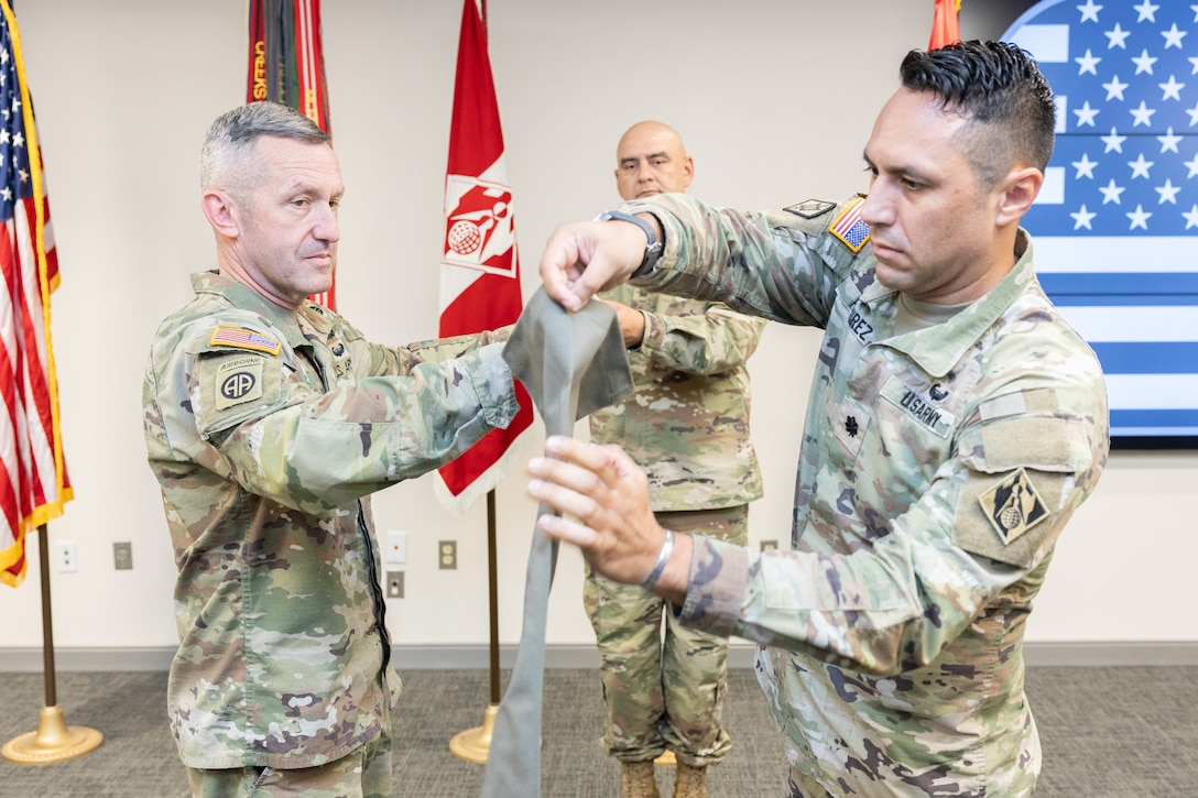 3 men in uniform rolling up the Expeditionary District flag.
