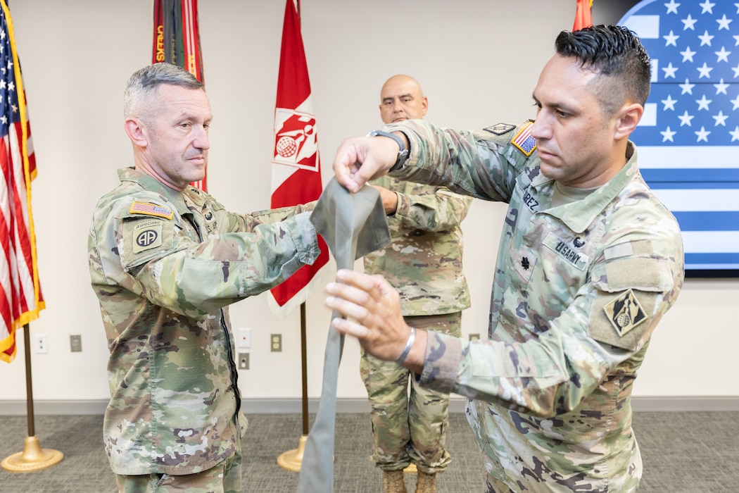 3 men in uniform rolling up the Expeditionary District flag.