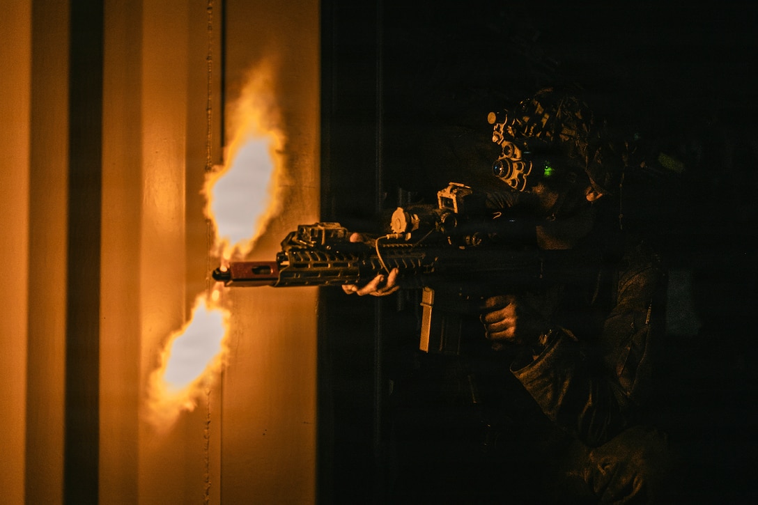 A soldier standing in the darkness fires a machine gun.