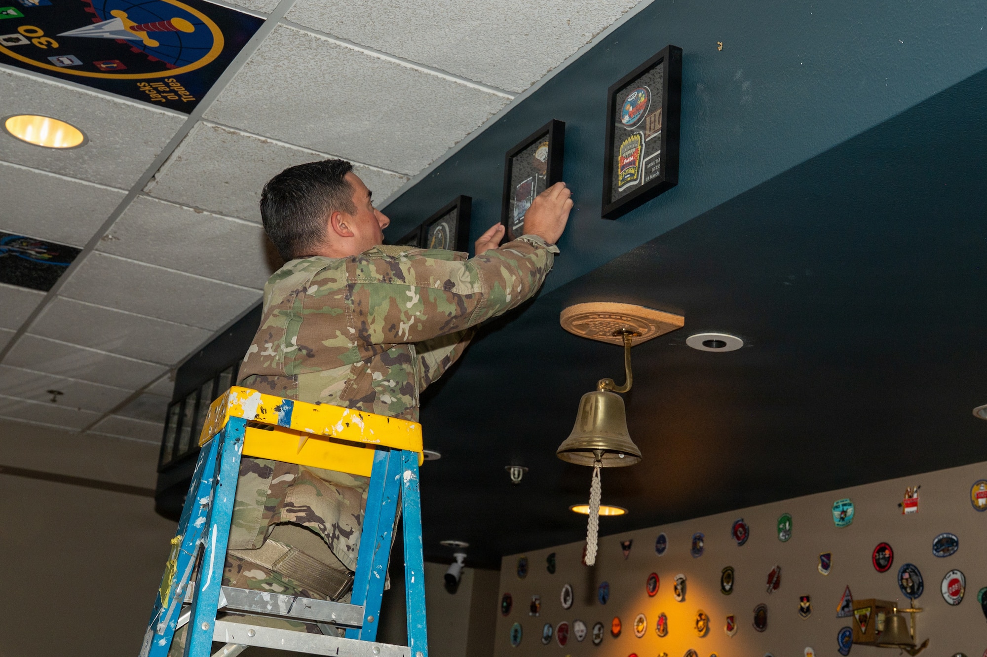 A person stands on a ladder and hangs up a patch frame on the wall.