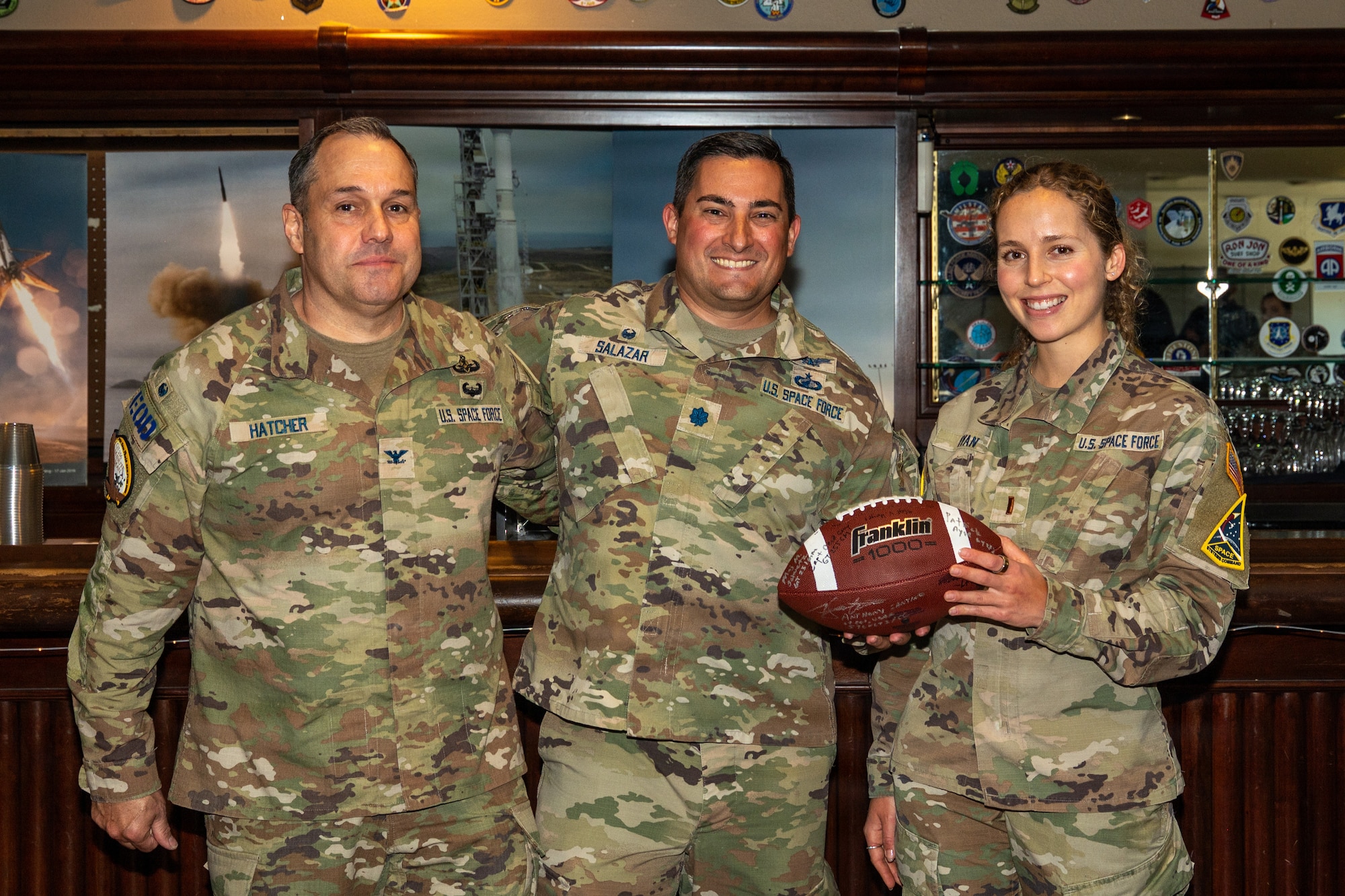 Three people stand and smile. One of them is holding a football.