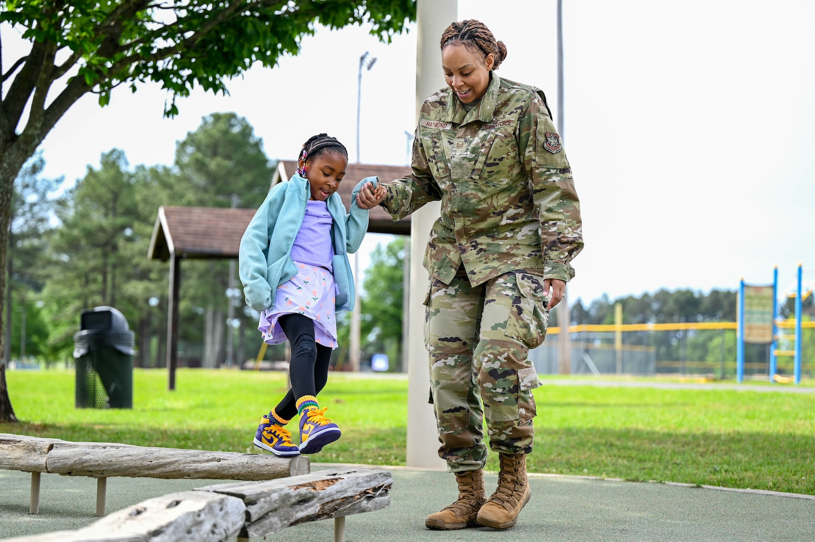 A woman helps a child walk across a balance beam.