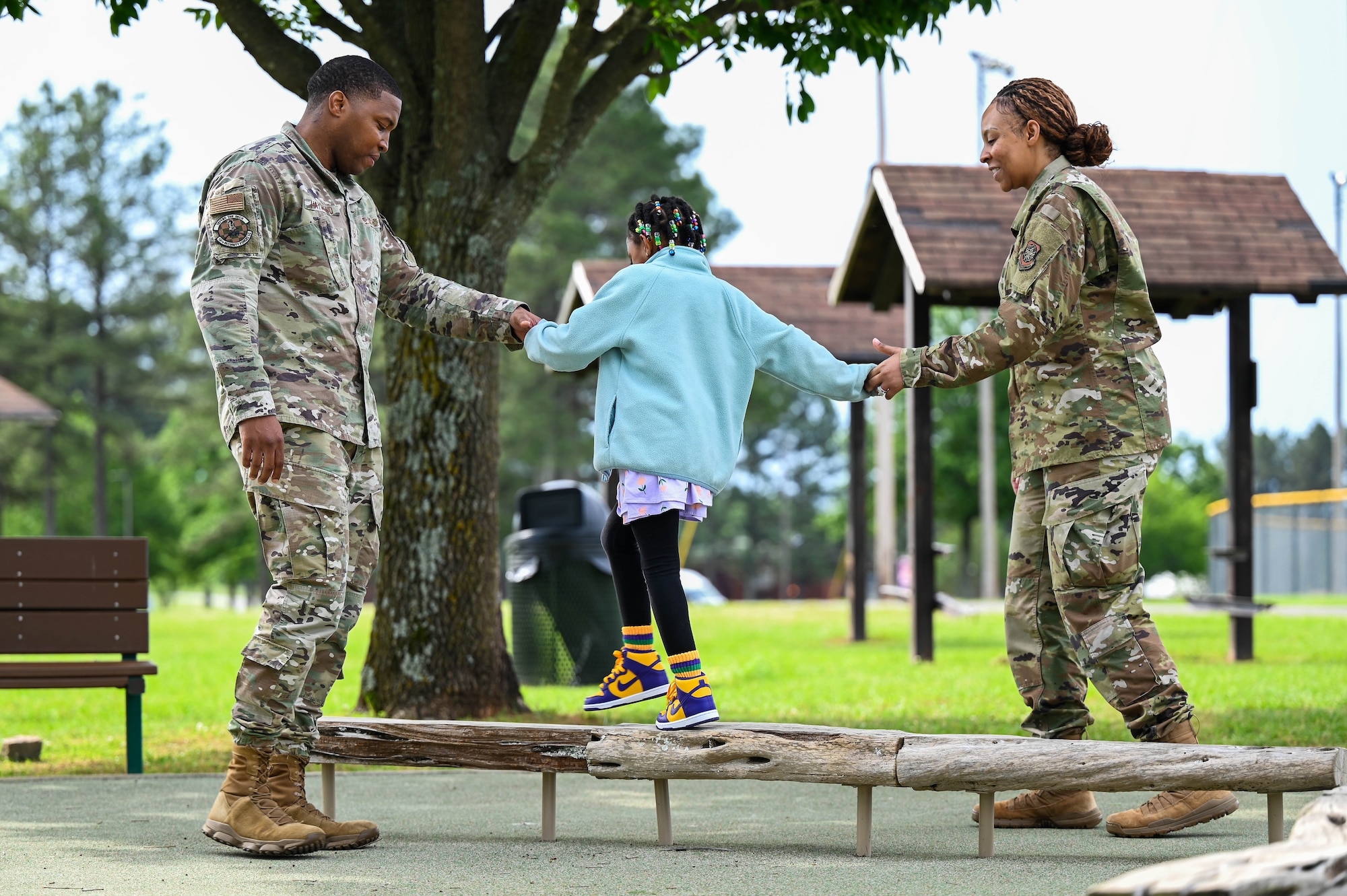 A man and women help a child walk across a balance beam.