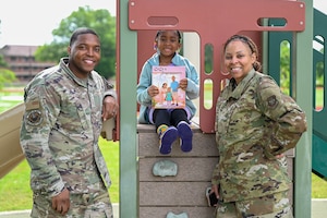 A man, woman and child stand in front of playground equipment smiling and posing for a photo.
