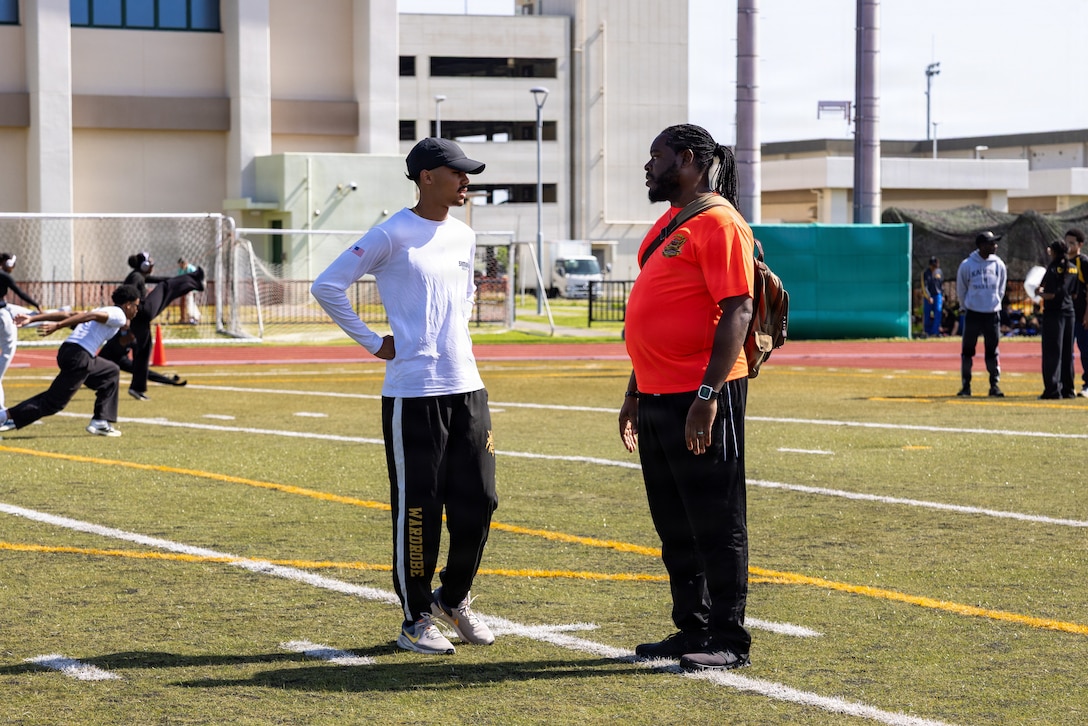 Jerron “JJ” Johnson, center right, the director of the Matthew C. Perry High School track and field team, speaks with one of his student athletes before the Department of Defense Education Activity Pacific Far East Championship 2026 track and field meet at Marine Corps Air Station Iwakuni, Japan, April 27, 2026. JJ also serves as the airfield manager for MCAS Iwakuni and was recognized for his contributions to the community through both his professional responsibilities and volunteer efforts. (U.S. Marine Corps photo by Cpl. Dahkareo Pritchett)