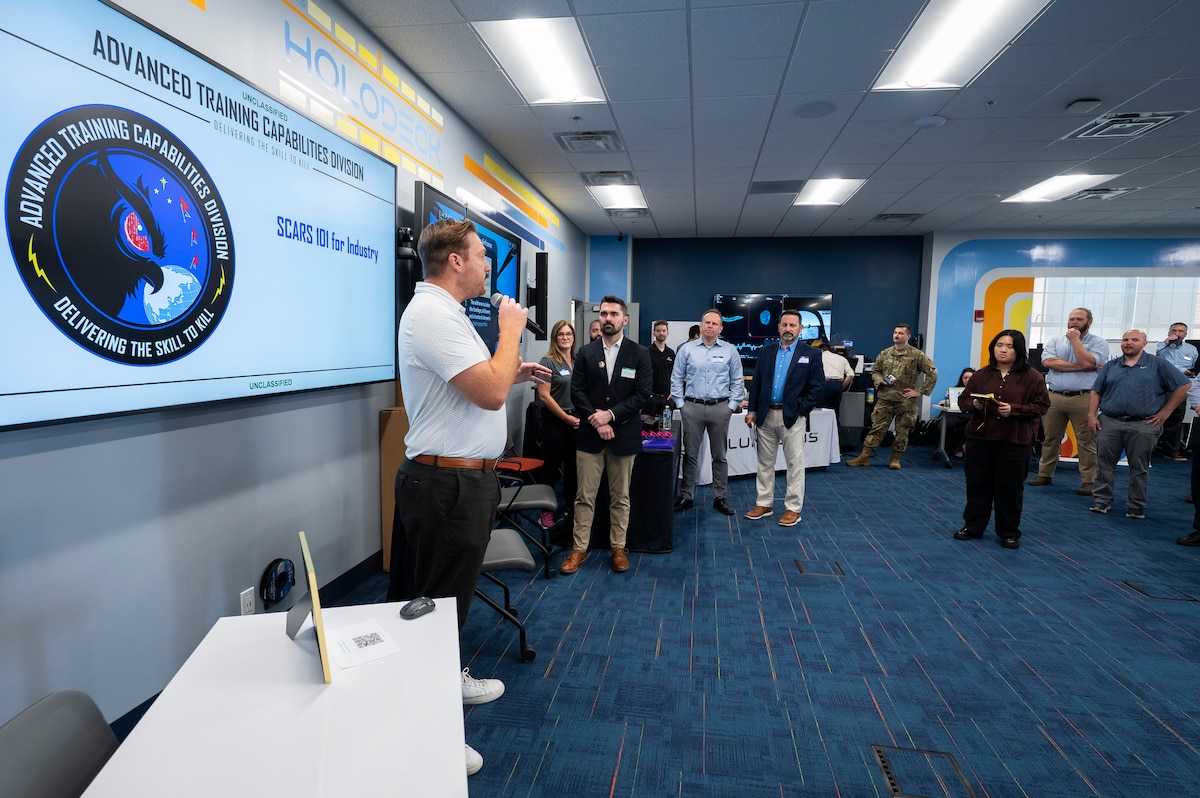 Individuals standing in front of large screen, listening to presentation.