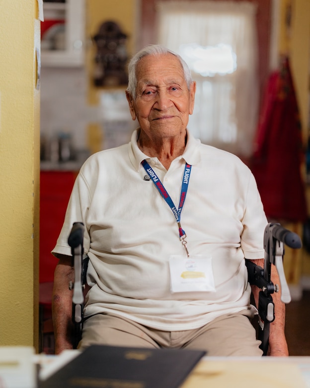 An older man with white hair sits in a wheelchair posing for a photo in a house.