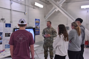 Staff Sgt. John Johnson, a 185th Air Refueling Wing public affairs specialist, stands with his hands clasped together and speaks to four visiting students.