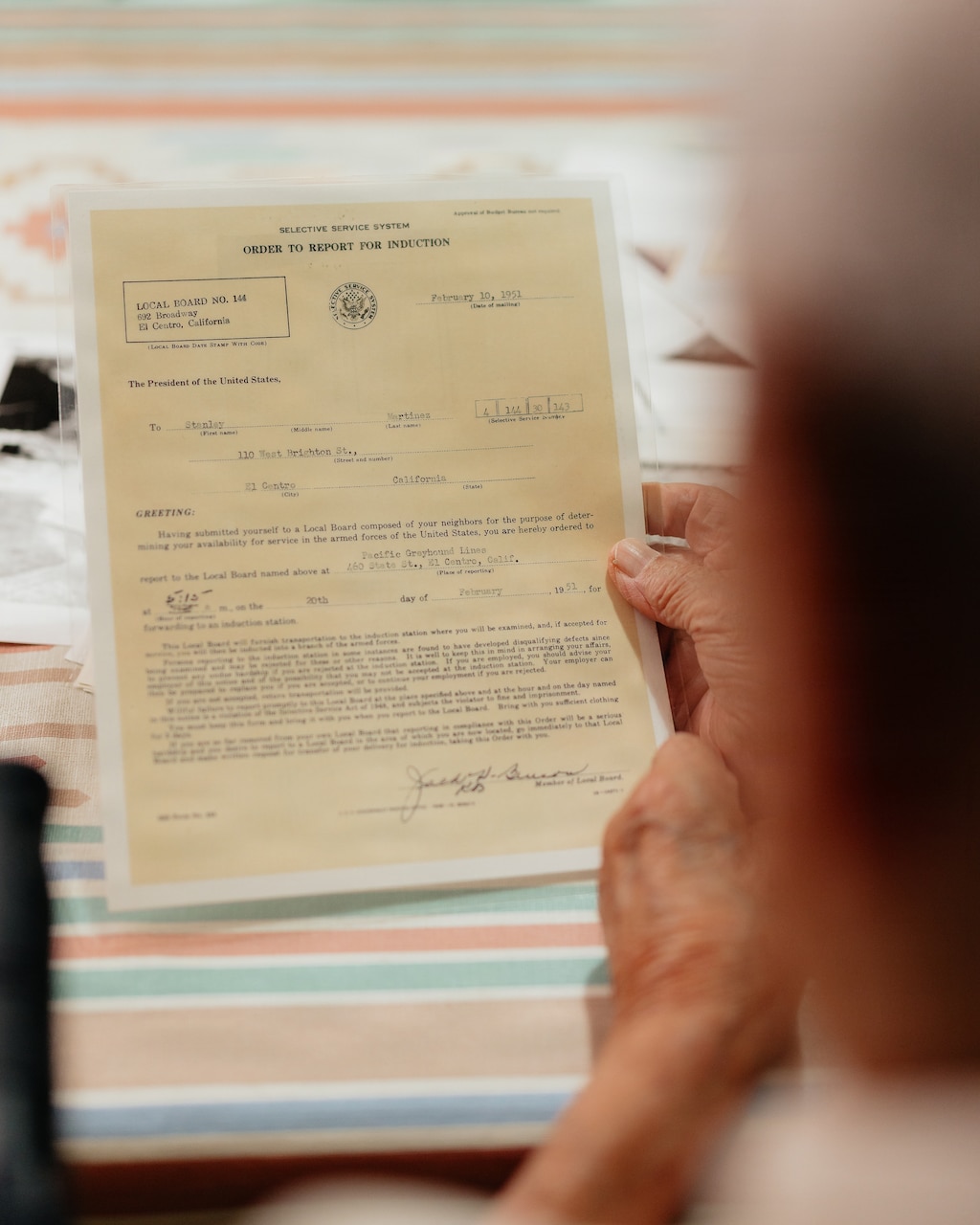An older man holds a military draft notice in his hand while sitting at a table.