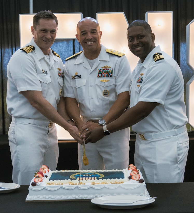 Three men cut a cake.