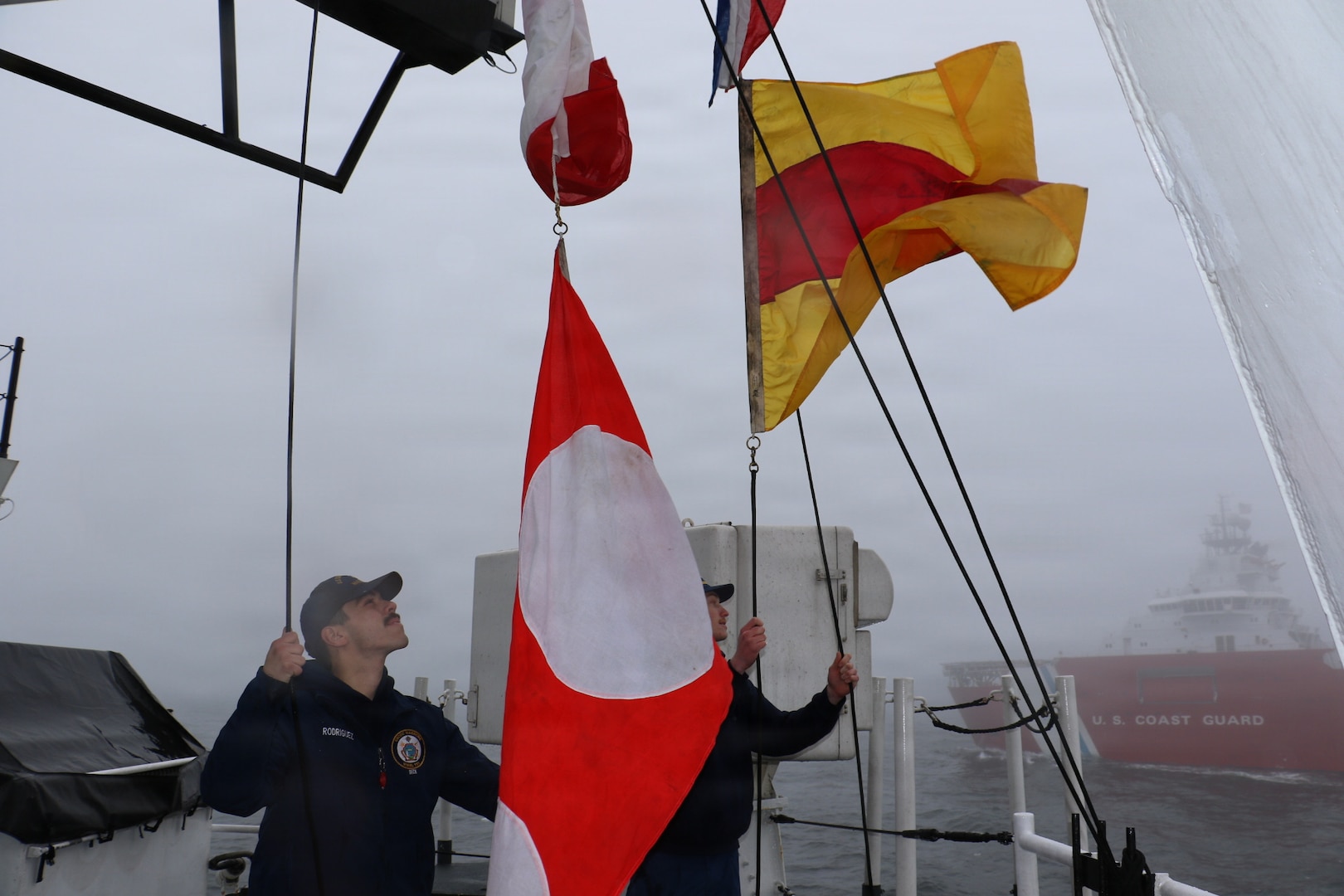 U.S. Coast Guard Petty Officer 2nd Class Jaiden Rodriguez and U.S. Coast Guard Petty Officer 3rd Class Donovan Weiss, crewmembers aboard USCGC Waesche (WMSL 751) hoist signal flags as part of a Passing Exercise and Visual Communications exercise with USCGC Storis (WAGB-21) in the Bering Sea, April 14, 2026. The primary mission of the patrol was the enforcement of fisheries laws to ensure the sustainability of our nation’s living marine resources. (U.S. Coast Guard photo by Petty Officer 3rd Class Lillian Escobar)