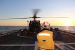 U.S. Coast Guard Ensign Garth Bowman, a landing signal officer assigned to U.S. Coast Guard Cutter Waesche (WMSL 751), directs an MH-60 Jayhawk helicopter from Air Station Kodiak during flight operations in the Bering Sea, Feb. 21, 2026. Training is essential to maintaining unit readiness and proficiency for Waesche and the air stations. (U.S. Coast Guard photo by Petty Officer 3rd Class Christian Swenk)