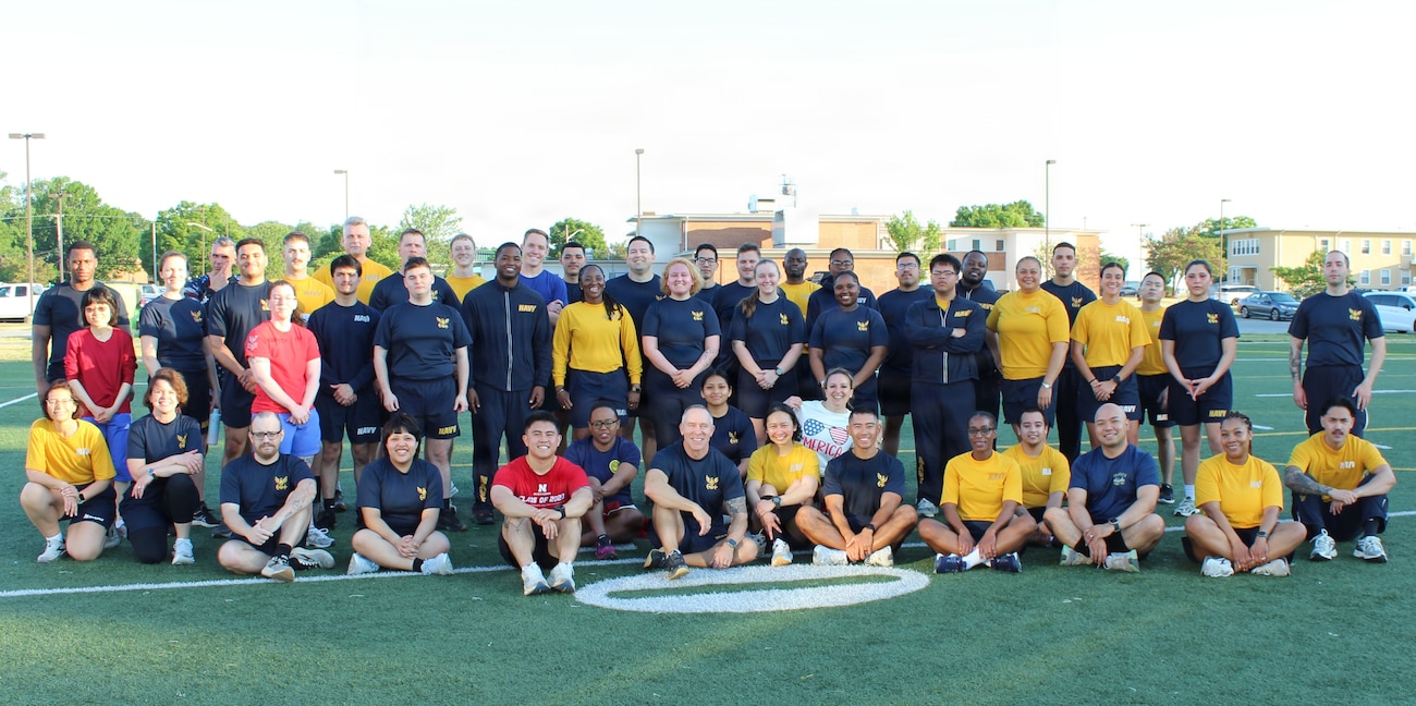 Service members assigned to Navy Medicine Readiness and Training Command (NMRTC) Patuxent River gather for a group photo at the Naval Air Station Patuxent River Drill Hall Field following the completion of the command’s monthly physical training event.

The command took on the 'Murph' challenge—consisting of a 1-mile run, 100 pull-ups, 200 push-ups, 300 squats, and a final 1-mile run—to honor the upcoming Memorial Day weekend and pay tribute to Navy SEAL Lt. Michael Murphy, who was killed in action in Afghanistan in 2005 and posthumously awarded the Medal of Honor.

To foster unit cohesion and ensure full participation, the grueling workout was modified into a team event, breaking Sailors into groups to partition the repetitions across a collective unit.