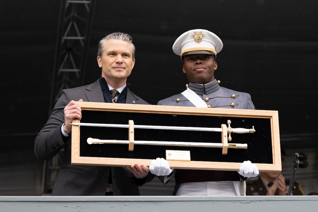 A man in business attire and a man in a formal military uniform hold a framed sword.