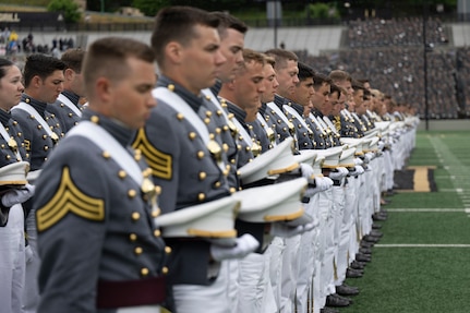 More than a dozen people in formal military uniforms bow their heads and holds their caps while standing in rows.