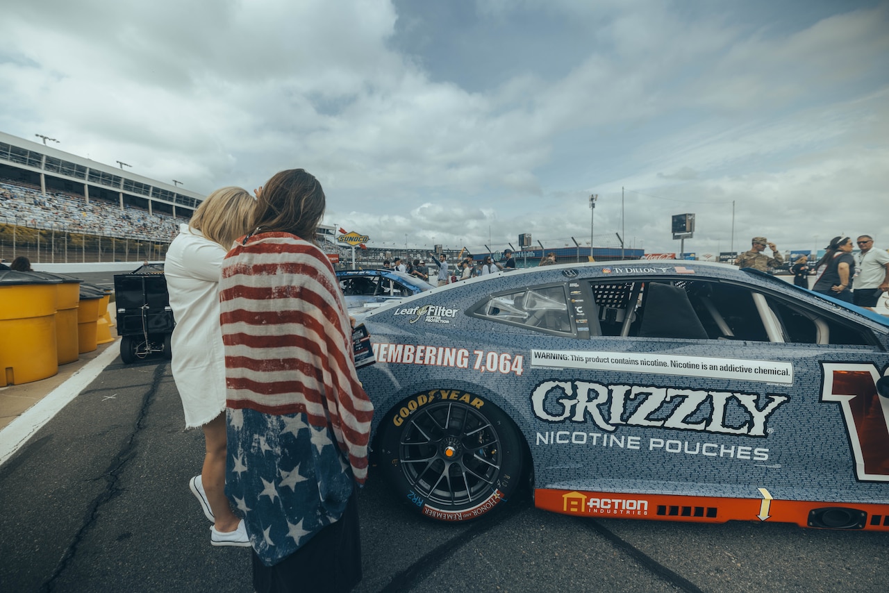 Two women in casual attire look at a race car parked on a track.