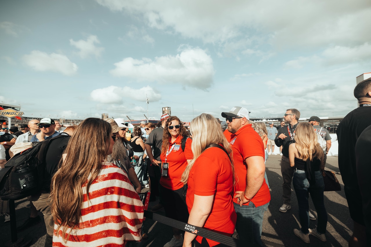 Dozens of people talk on a racetrack outside during daytime.