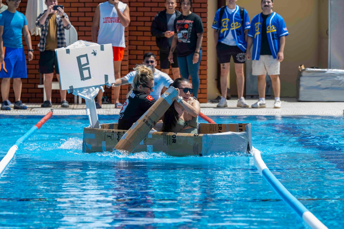 People in a cardboard make-shift boat paddle in a pool