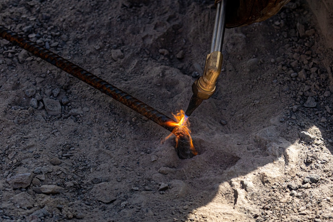 A close-up shot of a lit torch heating a metal rod, causing it to glow red-hot at the tip.