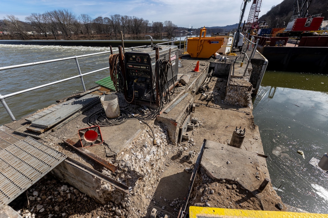 A view of a concrete pier under construction next to a river, with a welding machine and other equipment visible.