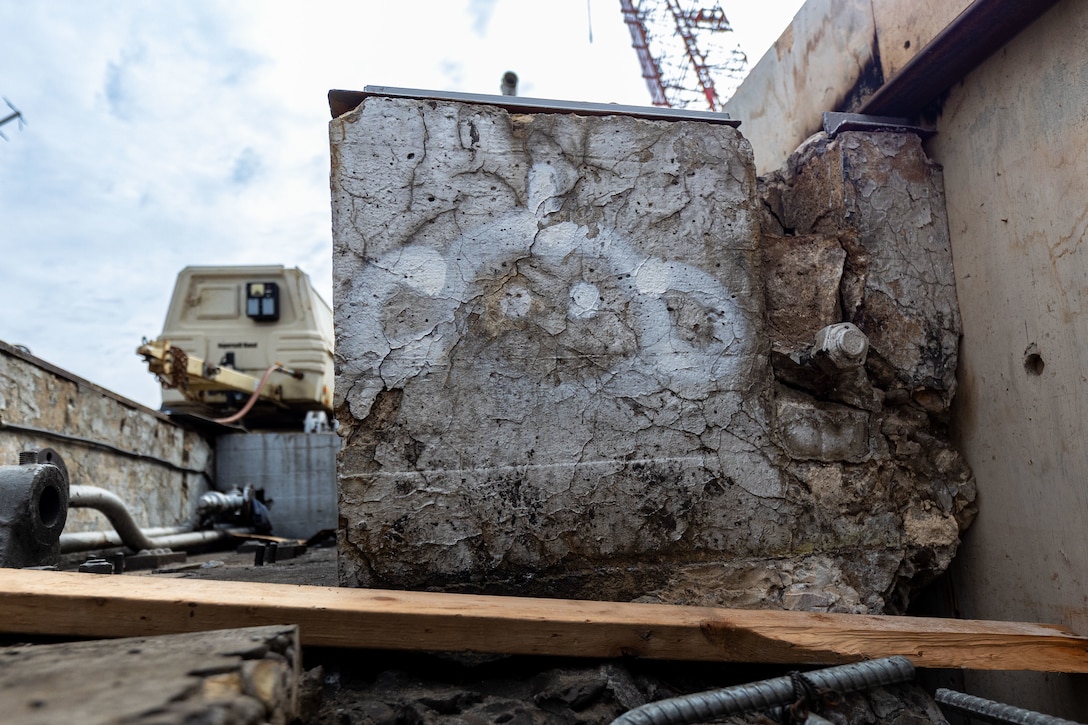 A close-up of a weathered and crumbling concrete block with white spray-painted markings.