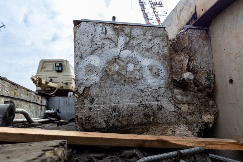 A close-up of a weathered and crumbling concrete block with white spray-painted markings.