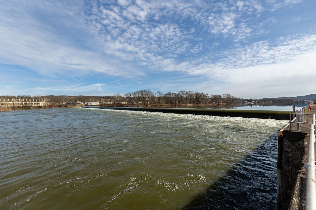 A wide shot of a river with a dam under a partly cloudy sky.
