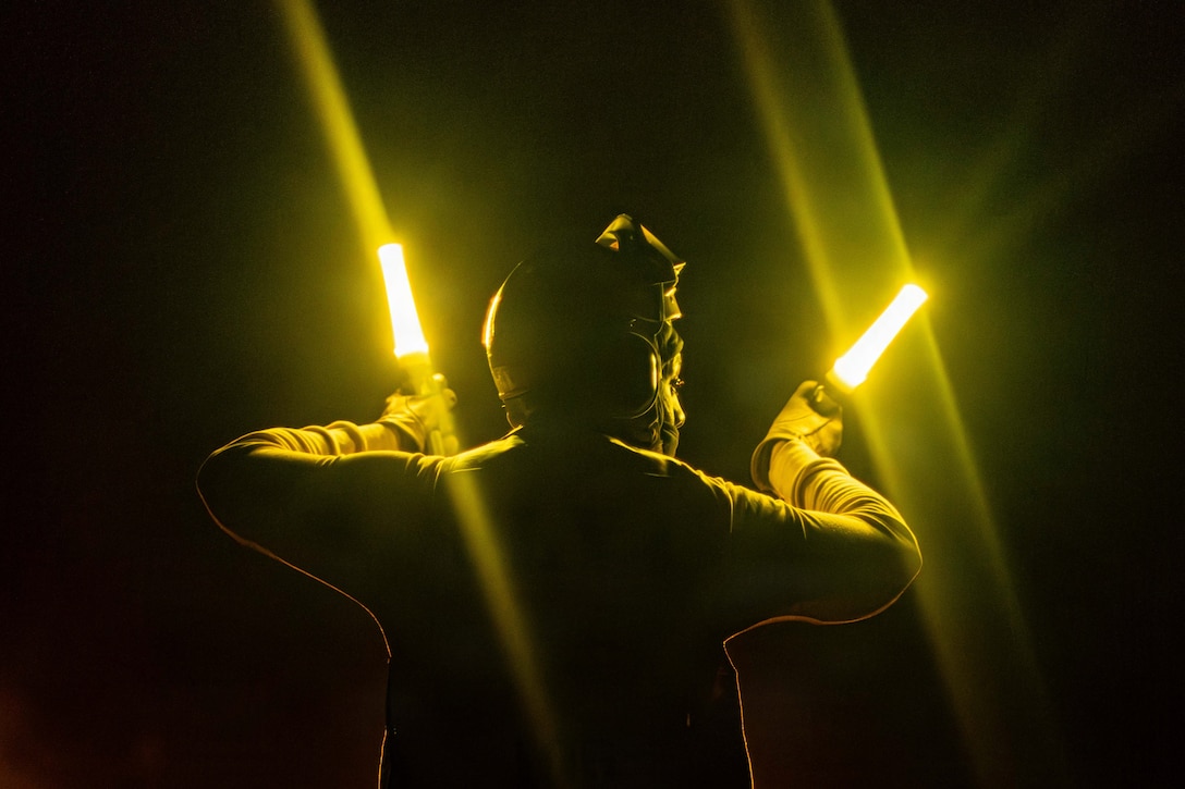 A sailor holds two neon yellow batons while standing in the dark.