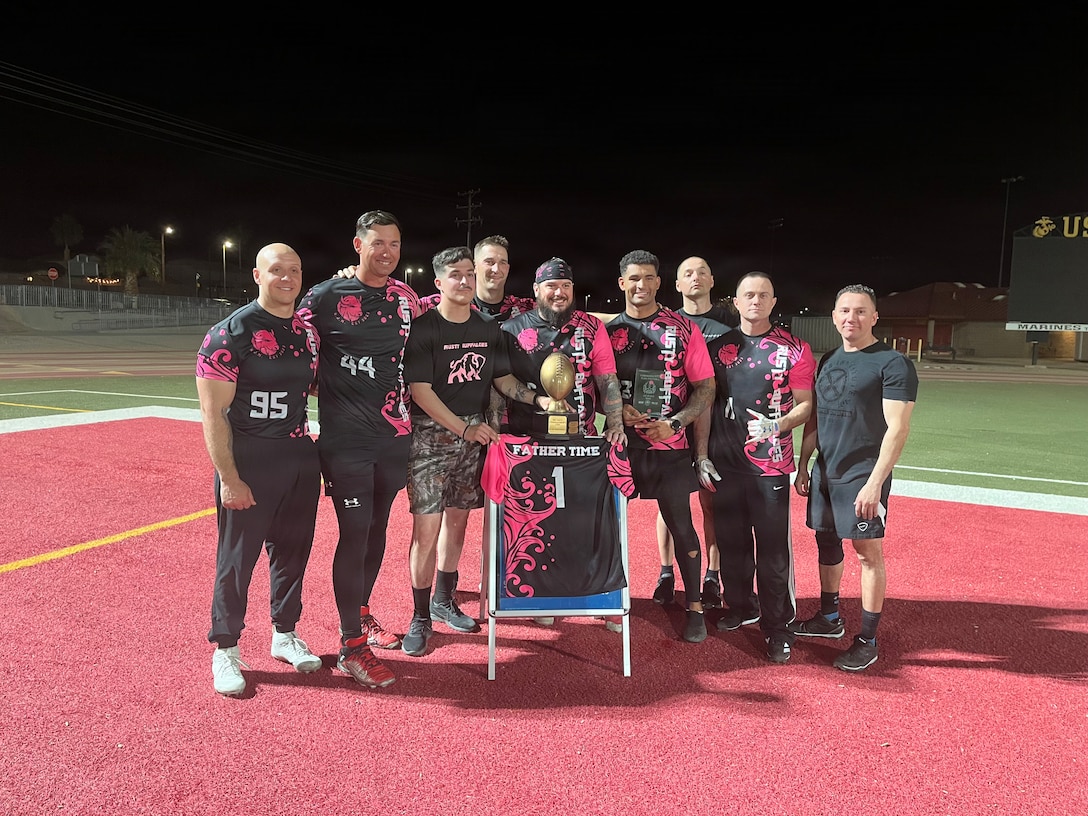 Marine Corps Logistics and Operations Group's flag football team, the Rusty Buffaloes, poses for a photo with the jersey of the late Gunnery Sgt. Robert McDonald, after winning the 2026 Commander's Cup Flag Football Championship, at Marine Corps Air Ground Combat Center, California, March 30, 2026.  The flag football team was originally formed in 2023 by McDonald. Though only six players from the original team formed by McDonald remain, the mission has never changed: every game is played in his honor and his impact is still felt across the team long after his passing.