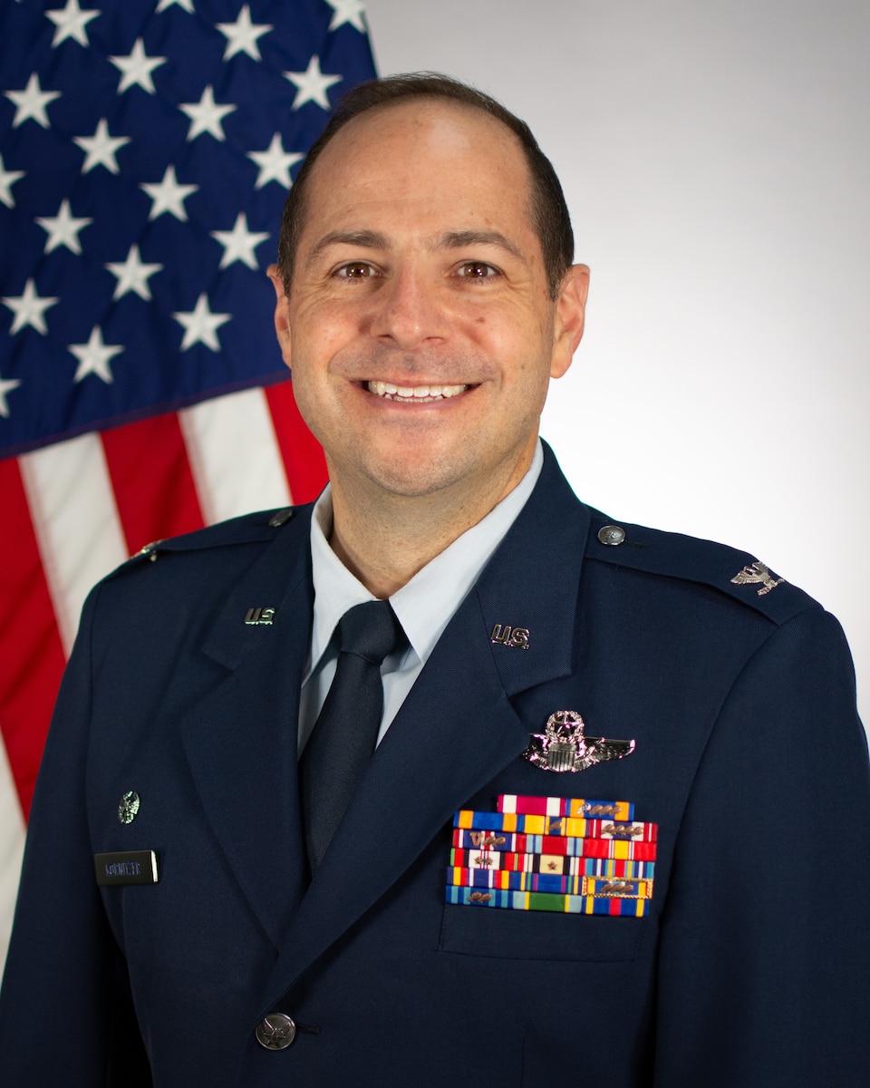 Service member poses for official portrait in front of US flag wearing their service dress blues