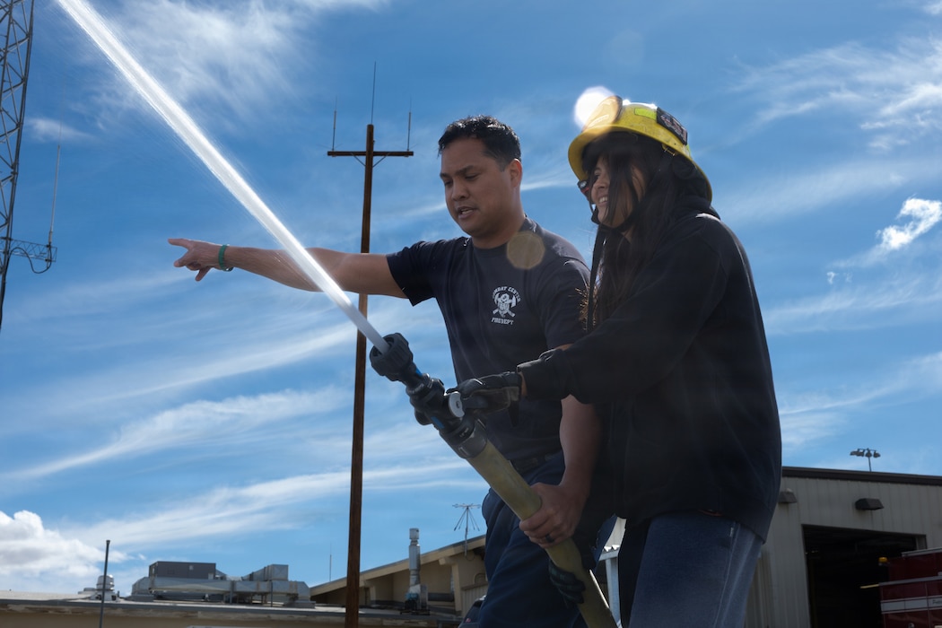 Joshua Gonzales, a fire inspector with the Combat Center Fire Department, demonstrates how to properly use a fire hose to a Morongo Unified School District student during the Job Shadowing event at Marine Corps Air Ground Combat Center, Twentynine Palms, California, May 5, 2026. The Job Shadowing program, students are paired with subject matter experts to get a closer look at the daily operations of various careers they are interested in exploring at the Combat Center. (U.S. Marine Corps photo by Pfc. Ethan DePaul)