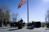 An Air Force officer speaks beneath a large U.S. flag outdoors.