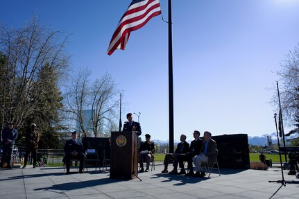 An Air Force officer speaks beneath a large U.S. flag outdoors.