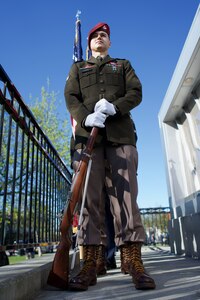 An Army Soldier wearing dress greens holds a rifle at order arms.