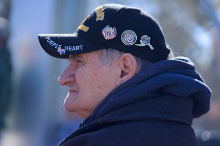 An older veteran with Vietnam War cap covered in military unit pins.