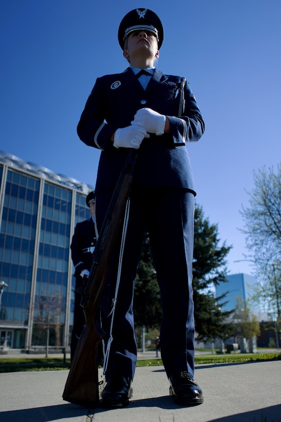 An Air Force Airman in dress blues holding a rifle at order arms.