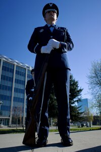 An Air Force Airman in dress blues holding a rifle at order arms.