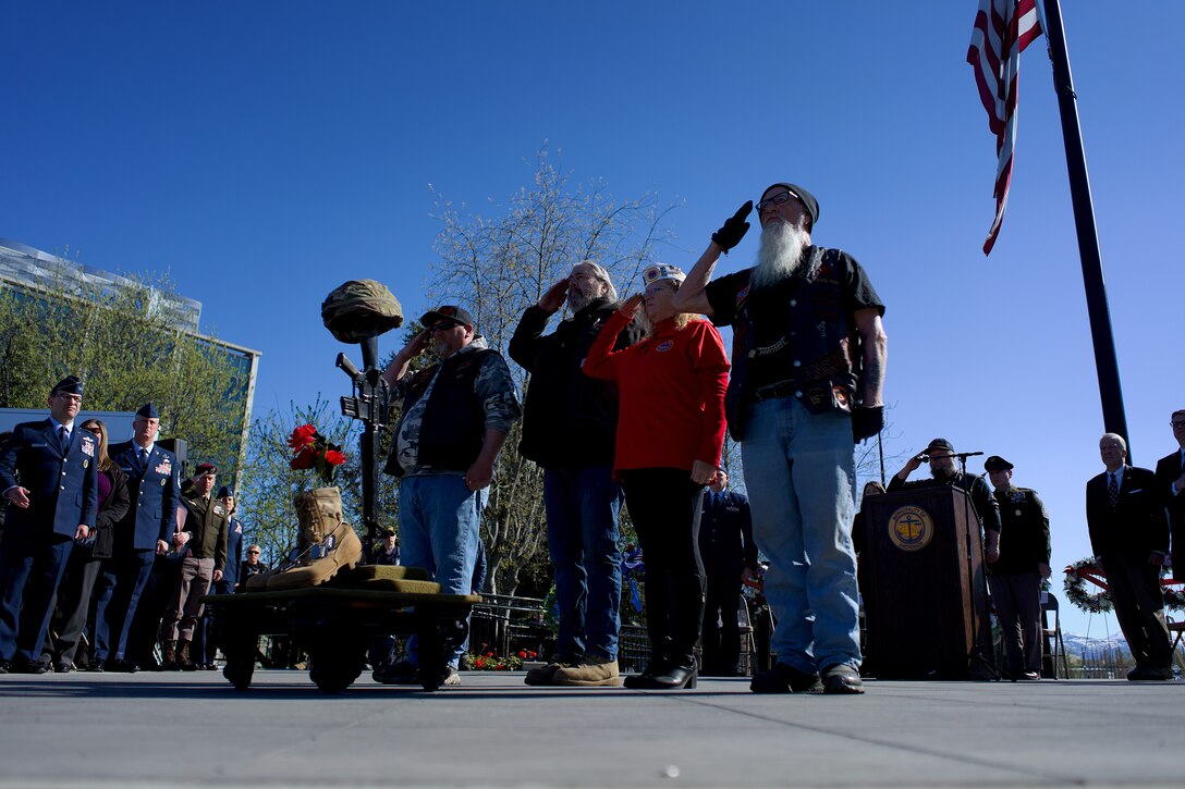 Veterans in biker outfits honoring a rifle, helmet, and dog tags memorial