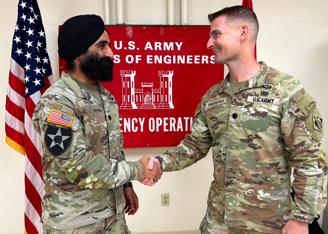 A man in an Army uniform shakes the hand of another man in an Army uniform in front of a large banner that reads "U.S. Army Corps of Engineers Emergency Operations."