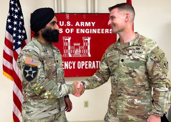 A man in an Army uniform shakes the hand of another man in an Army uniform in front of a large banner that reads "U.S. Army Corps of Engineers Emergency Operations."