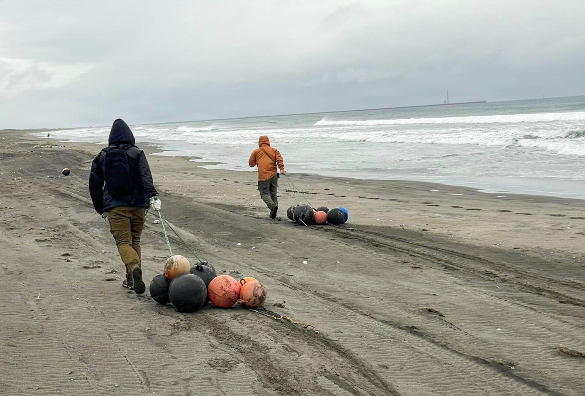 U.S. Air Force Staff Sgt. Stephen Terrick, left, 13th Fighter Generation Squadron maintenance manager, and Senior Airman Alberto Rodriguez, 509th Maintenance Squadron aircrew egress systems journeyman, drag buoys across the beach during a cleanup.