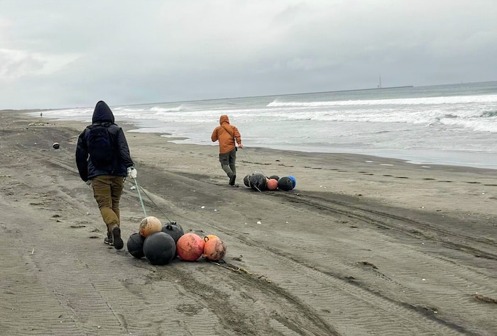 U.S. Air Force Staff Sgt. Stephen Terrick, left, 13th Fighter Generation Squadron maintenance manager, and Senior Airman Alberto Rodriguez, 509th Maintenance Squadron aircrew egress systems journeyman, drag buoys across the beach during a cleanup.