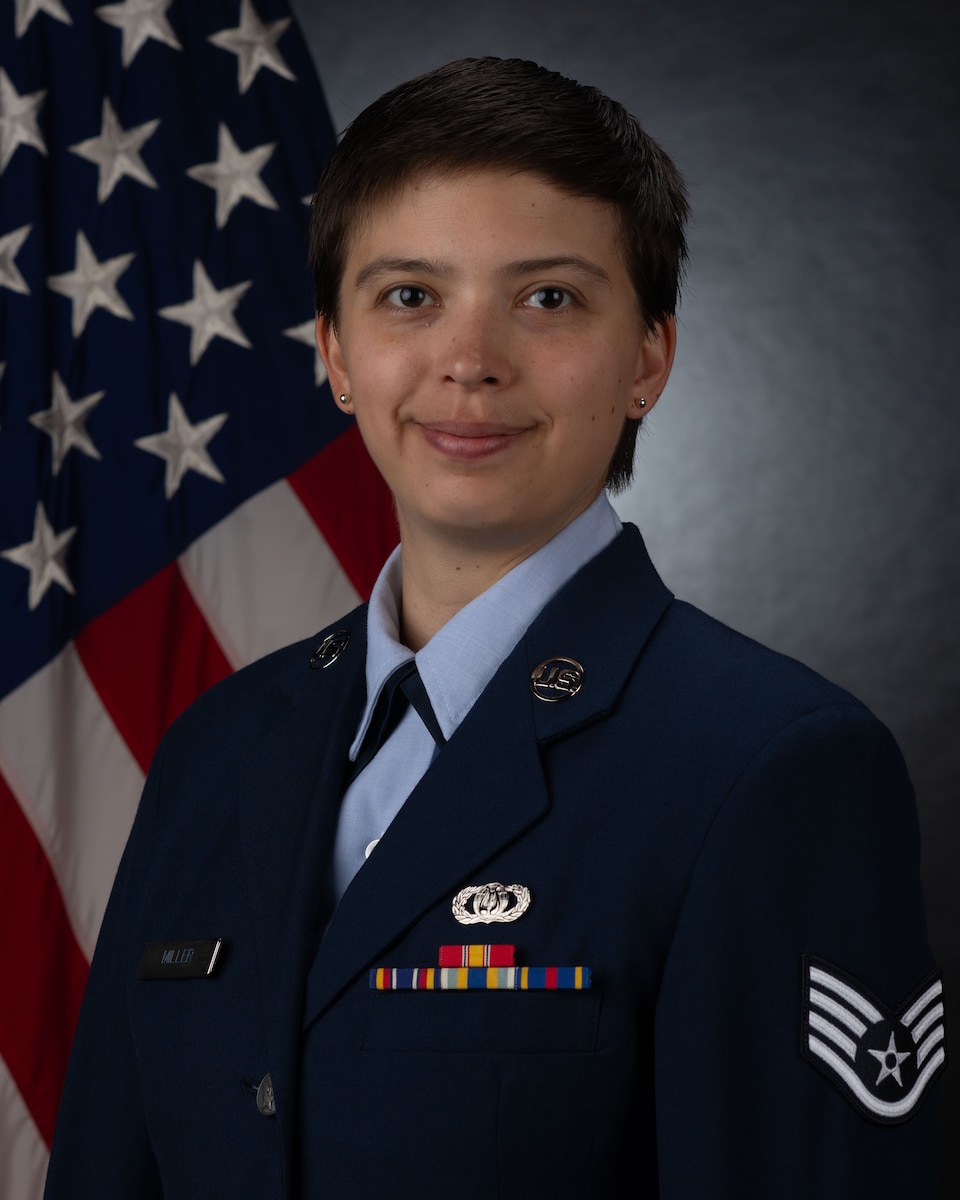 Official photo of Staff Sergeant Jordan Miller, horn, United States Air Force Bands. SSgt Miller is wearing navy blue service dress in front of an American flag.