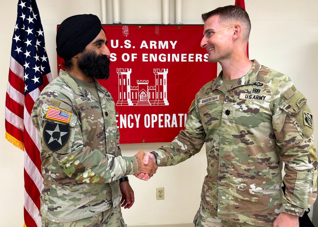 A man in an Army uniform shakes the hand of another man in an Army uniform in front of a large banner that reads "U.S. Army Corps of Engineers Emergency Operations."