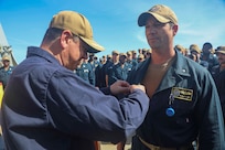 Capt. Alex Mamikonian (left), Naval Surface Group Europe, pins Cmdr. R. J. DaPrato, incoming commanding officer of USS Roosevelt (DDG 80), with the command-at-sea pin during a change of command ceremony on the flight deck of Roosevelt, May 22, 2026. Daprato relieved Cmdr. Jared L. Carlson from command of Roosevelt during the ceremony.