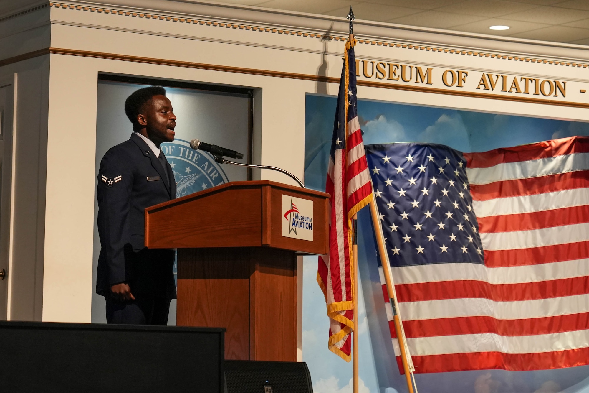 Man in military uniform sings the Star Spangled Banner at a podium